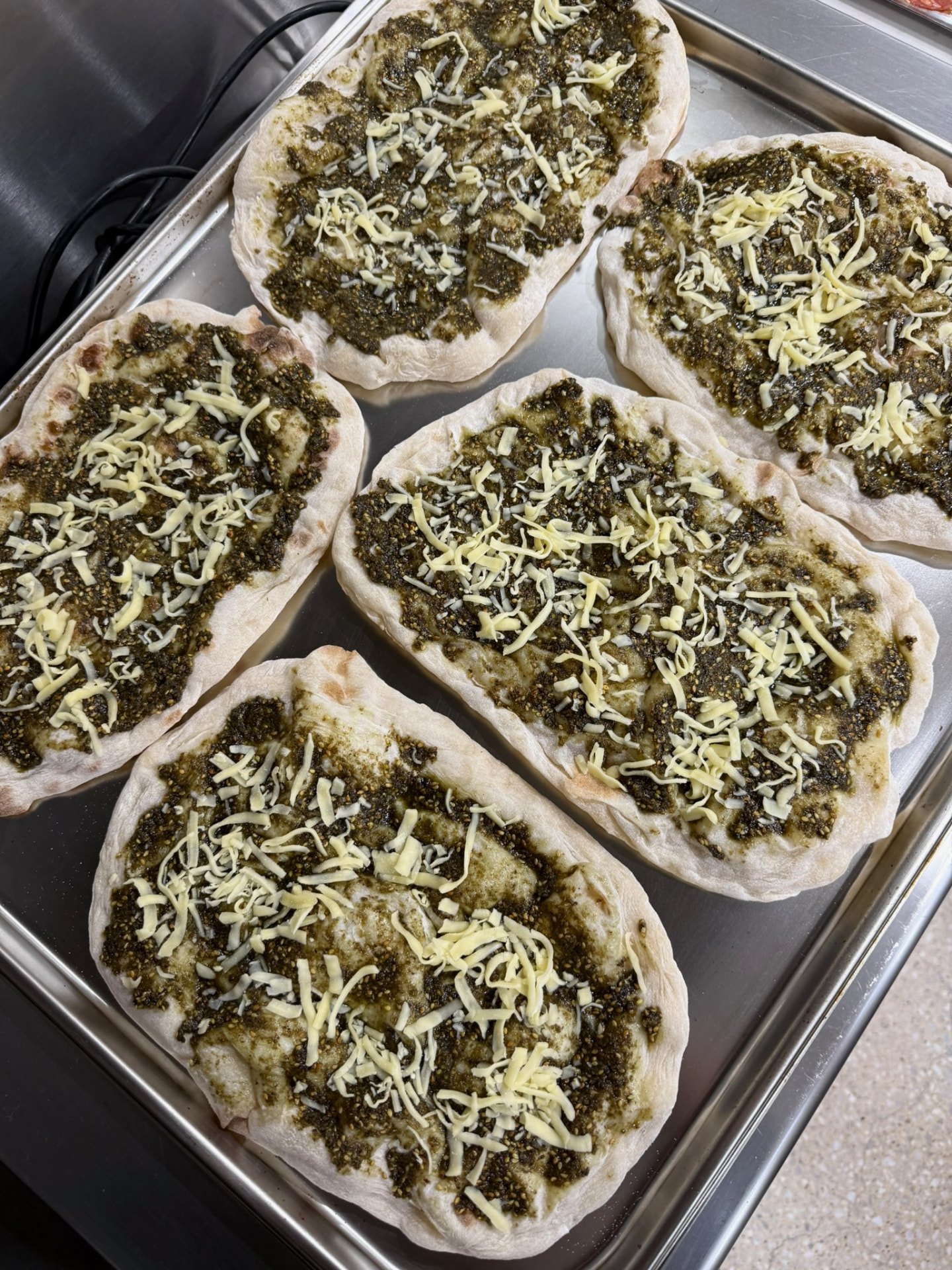 Five za'atar and cheese pinsa bases ready on a baking tray